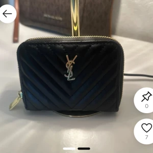 Svart quiltad plånbok från Saint Laurent - Snygg svart plånbok från Saint Laurent med guldiga detaljer och YSL-logga framtill. Plånboken är quiltad i ett V-mönster och har dragkedja runtom. Insidan har flera fack för kort och sedlar. Perfekt accessoar för dig som gillar lyxig och stilren design.