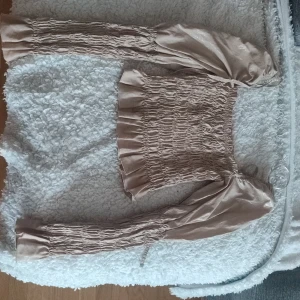 Beige omlott blus med puffärm Ny - Trendig beige blus med smockad kropp och långa puffärmar. Sidenliknande material ger en lyxig känsla och toppen har omlott-detalj vid axlarna. Perfekt för dig som gillar romantisk och chic stil. Aldrig använd. Endast testad utan prislapp 