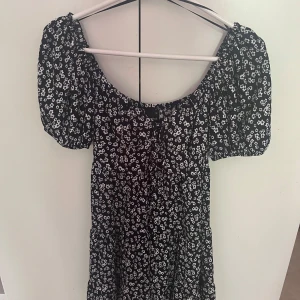 Marinblått blommig kortklänning Gina Tricot - Supersöt svart kortklänning från Gina Tricot med vita små blommor. Klänningen har puffiga korta ärmar, smockad resår vid axlarna och en lätt utställd kjol. Perfekt för en solig dag ☀️☀️ Använt en gång och de va på en skolavslutning, efter de så har de vart liggandes i min garderob💙