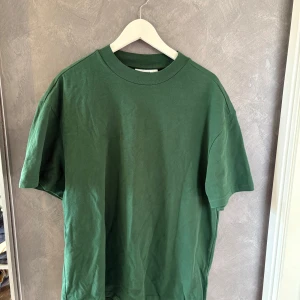 Grön basic t-shirt i bomull från WEEKDAY  - Enkel grön t-shirt med rund hals och korta ärmar. Modellen är rak och lite loose fit, perfekt för en chill och avslappnad stil. Tillverkad i mjuk bomull som känns skön mot huden. Inga tryck eller mönster, bara clean och stilren.