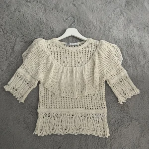 Stickad blus med volang från Zara - Superfin stickad blus från Zara i ljusbeige med volangdetalj över axlarna och bröstet. Blusen har trekvartsärm och ett vackert virkat mönster som ger en boho-vibe. Perfekt till vår och sommar för en chill men ändå söt look. Säljs inte längre på Zara, köpt för 400-500 kr, men säljer då för 250, aldrig använd så väldigt bra skick!