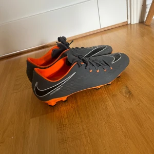 Nike fotbollsskor grå/orange - Säljer ett par Nike fotbollsskor i grått med orange detaljer och innersida. Perfekta för dig som vill sticka ut på planen med snygg design och bra passform. Storlek 44