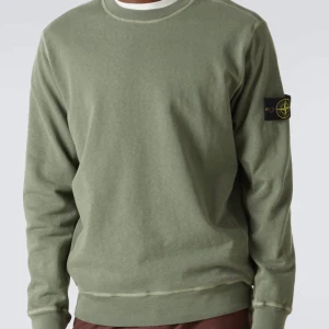 Grön Stone Island sweatshirt - Säljer en grön sweatshirt från Stone Island med klassisk patch på ärmen. Tröjan har rund halsringning, ribbade muddar och är tillverkad i mjuk bomull. Perfekt för dig som gillar streetwear och vill ha en clean look med ikonisk detalj. Defekter finns på sista bilderna