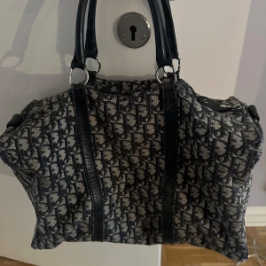  Äkta Dior monogram handväska i canvas - Säljer en klassisk äkta handväska från Dior äkta från 1980talet det är en vintage väska med ikoniskt monogrammönster i svart och beige. Väskan har dubbla svarta handtag i skinn och dragkedja upptill. Perfekt storlek för att få plats med allt du behöver och ger en lyxig vibe till din outfit.