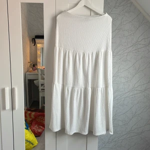 Vit långkjolfrån Gina Tricot - Superfin vit långkjol från Gina Tricot i storlek M. Kjolen har en luftig, volangig design med struktur i tyget och en avslappnad passform. Perfekt för varma dagar och enkel att styla med sneakers eller sandaler.