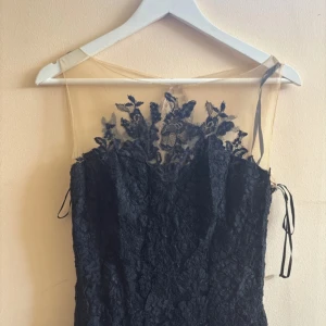 Svart spetsklänning från Pronovias - Säljer en elegant långklänning från Pronovias i svart spets med blommiga broderier. Klänningen har transparent mesh upptill, knappar längs ryggen och smala band i sidorna. Perfekt för dig som vill sticka ut med en klassisk och sofistikerad look.Hade den bara på en fest så det är tip ny har köpt den för 9000kr