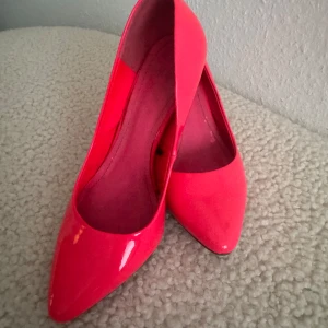 Neonrosa pumps med spetsig tå - Snygga neonrosa pumps från H&M med glansig finish och spetsig tå. Skorna har smal klack och en klassisk siluett som verkligen sticker ut. Perfekta för dig som vill ha en färgklick till outfiten. Lite skavanker, se sista två bilder.