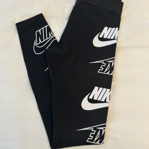 Svarta träningsleggings med logga från Nike  - Svarta träningsleggings med stora vita loggor tryckta längs benen från Nike i storlek XS. Tight passform och stretchigt material som sitter skönt. 