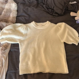 Krämvit stickad tröja Gina Tricot - Superfin krämvit stickad tröja från Gina Tricot med puffiga korta ärmar och ribbade muddar. Använd fåtal gånger . Kan absolut sänka pris vid snabbt köp.Tryck gärna på köp nu.