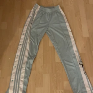 Adidas ljusblå träningsbyxor XS - Snygga ljusblå träningsbyxor från Adidas med vita sidor och klassiska tre ränder längs benen. Byxorna har tryckknappar längs hela sidorna och resår i midjan. Perfekta för en sportig look eller chill outfit.