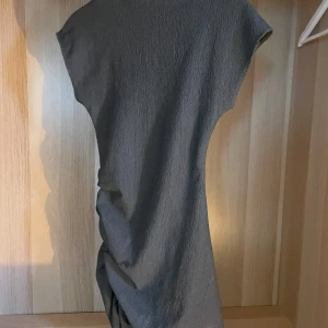 Grå kort klänning - En grå, tight och kort klänning med ribbad struktur. Klänningen har korta ärmar och en lite hög hals, samt en figurnära passform som framhäver siluetten.🥰Använd endast två gånger