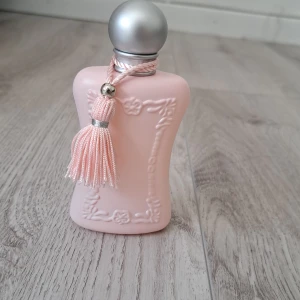 Parfums de Marly Delina EdP 75ml - Delina Eau de Parfum i en lyxig, matt ljusrosa flaska med silverfärgat klotlock och dekorativ tofs. Flaskan levereras i matchande rosa kartong. Feminint och elegant intryck. Är helt ny, oanvänd då jag inte tycker att doften passar mig.