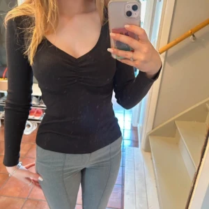 Svart ribbad topp från Old Navy - Svart långärmad topp från Old Navy i ribbad bomullsmix. Snygg v-ringning med rynkdetalj framtill som ger en cool touch. Figurnära passform som sitter snyggt och är perfekt till jeans eller kjol.