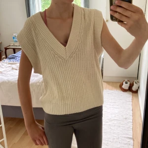 Beige stickad väst från Gina Tricot - Superfin beige stickad väst från Gina Tricot i storlek XS. Västen har bred ribbstickning, djup v-ringning och är ärmlös med en lite boxig passform. Perfekt att slänga över en skjorta eller t-shirt för en trendig lager-på-lager-look.