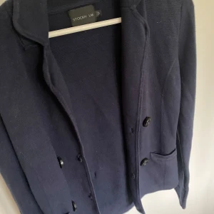 Mörkblå stickad kavaj från Stockh LM - Snygg mörkblå stickad kavaj från Stockh LM med klassisk krage, knappar framtill och fickor. Perfekt för dig som vill ha en stilren och bekväm look. Passar lika bra till jeans som till kostymbyxor.