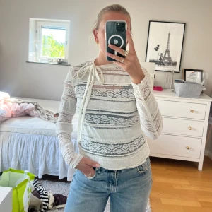 Vit spetsblus med knyt i halsen - Supersöt vit blus i spets med lång ärm och coolt knytband vid halsen. Blusen har genomgående broderade detaljer i tyget. Älskar denna top men måste sälja bort lite kläder 🥹kan mötas i stockholm city annars står köparen för frakten!