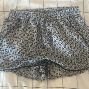 Svartvita mönstrade shorts Monki S - Shorts från Monki i storlek S med svartvitt abstrakt mönster. De har elastisk midja och snörning framtill för extra komfort. Lätta och luftiga, perfekta för varma dagar. Materialet känns som polyester och passformen är loose.