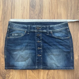 Mörk jeanskjol med knappar från Mango Jeans - Snygg mörkblå jeanskjol från Mango Jeans. Kjolen är kort och har knapp detaljer. Perfekt till sommaren! Kan ha både low waist passform och midwaist. Stretchigt tyg! Storleken ör 38 men hade sagt att den sitter som 36 (S). Hör av er vid frågor!