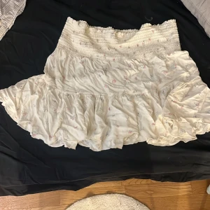 Vit blommig volangkjol från 157 - Supersöt kort kjol i vitt med små blommor i rosa och blått från 157. Kjolen har bred smock i midjan och volang nertill. Perfekt för dig som gillar romantisk och chill stil. !Köpare står för frakt!