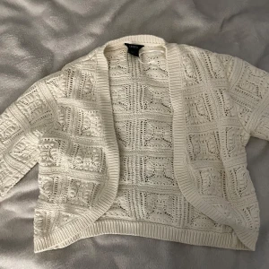 Vit stickad kofta från Lindex - Superfin vit stickad kofta från Lindex i storlek S. Koftan har ett snyggt virkat mönster med ribbade kanter och öppen front. Perfekt att slänga över en topp för en chill och trendig look.