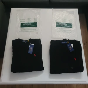 2 st svarta tröjor från Polo Ralph Lauren - Kabelstickad svart tröja från Polo Ralph Lauren med rund halsringning och klassisk röd broderad logga på bröstet. Tröjan är långärmad och har ribbade muddar vid ärmslut och nederkant. Perfekt för dig som gillar stilren och tidlös design. En är i storlek M och en är i storlek S. Du kan såklart köpa den separat också 🤗