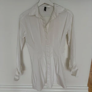 Vit långärmad skjortklänning från H&M Divided - Klassisk vit skjortklänning från H&M Divided i storlek 32. Skjortan har lång ärm, krage och knäppning framtill. 