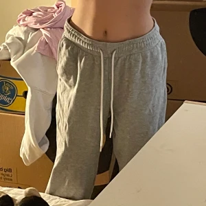 Grå mjukisbyxor från H&M Basics - Grå mjukisbyxor från H&M Basics i storlek M. De har resår i midjan med vit snörning och raka ben. Tillverkade i mjuk bomullsblandning, perfekta för chill dagar. Klassisk och enkel stil med sidfickor.