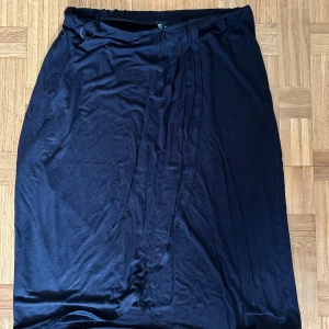 Svart omlottkjol från PIECES XL - Svart långkjol från PIECES i omlottmodell. Kjolen har en enkel och stilren look med mjukt fall och resår i midjan. Perfekt för dig som gillar minimalistisk stil och vill ha något bekvämt men ändå snyggt.