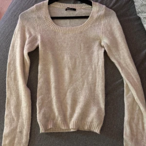 Beige stickad tröja från Gina Tricot - Mysig beige stickad tröja från Gina Tricot med rund halsringning och långa ärmar. Tröjan har ribbade muddar vid ärmslut och nederkant, perfekt för lager på lager under kyliga dagar.