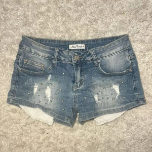 Blå jeansshorts med nitar från Nice Toxik - Snygga blå jeansshorts från Nice Toxik med slitna detaljer och silverfärgade nitar framtill. Shortsen har klassisk femficksmodell, bälteshällor och vit spetskant som sticker ut nedtill. Perfekta för sommaren och ger en cool vibe till din outfit. Köp via Swish + frakt (ej köp nu) eller direkt via vinted @moa.06 (pga plicks nya avgifterk) 🩷