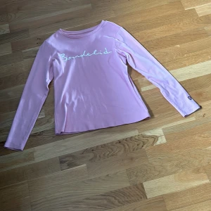 Rosa långärmad tröja från Bondelid - Snygg rosa långärmad tröja från Bondelid med vit broderad logga framtill och ett litet sköldmärke på ärmen. Tröjan är i mjuk bomull och har en klassisk passform. Storleken är S och är oanvänd. Nypris 599kr och säljes för 400kr.