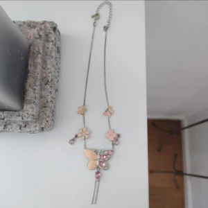 Sött halsband med fjäril och blommor - Supergulligt halsband med silverfärgad kedja, dekorerat med ljusrosa blommor och en stor fjäril med rosa stenar. Perfekt accessoar för dig som gillar söta detaljer och pastellfärger.