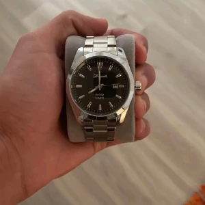 Silverfärgad  herrklocka från Doventi  - Stilren herrklocka från Doventi med svart urtavla och datumvisning. Klockan har en klassisk rund form och länkarmband i silverfärgat metall. Perfekt accessoar för dig som gillar en clean och tidlös look.