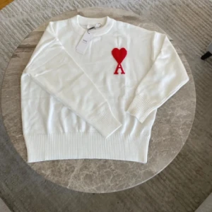 Vit stickad tröja från Ami Paris - Vit stickad tröja från Ami Paris med röd hjärtlogga och bokstaven A på bröstet. Tröjan har rund halsringning, ribbade muddar och är långärmad. Perfekt för dig som gillar stilrena plagg med en twist.