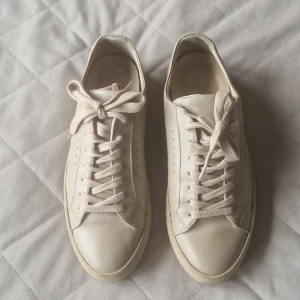 Vita sneakers i skinn från Filippa K - Stilrena beiga sneakers från Filippa K i mjukt skinn med klassisk rund tå och platt sula. Skorna har diskreta hål längs sidorna och vita bomullssnören. Perfekta för en clean och minimalistisk look.