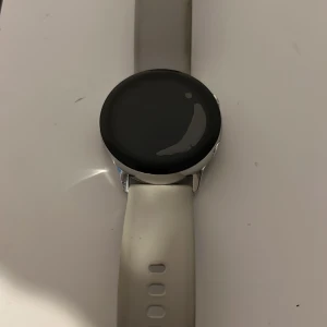 Samsung Galaxy Watch Active silver - Snygg Samsung Galaxy Watch Active med rund svart urtavla och silverfärgad ram. Klockan har ett stilrent vitt silikonarmband och kommer med laddkabel. Perfekt för dig som vill ha koll på träning och hälsa direkt på handleden. Med följer med en skärmskydd
