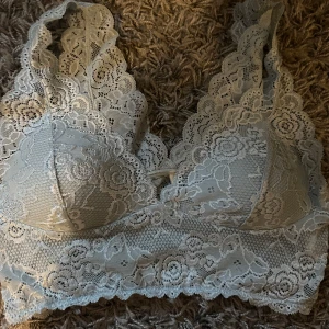 Ljusblå spetsig bralette topp - Supersöt ljusblå bralette topp i spets med blommigt mönster. Djup v-ringning och bred spetskant både upptill och nedtill. Ärmlös modell med breda axelband och mjuk, stretchig känsla. Perfekt att styla under en skjorta eller till höga jeans.