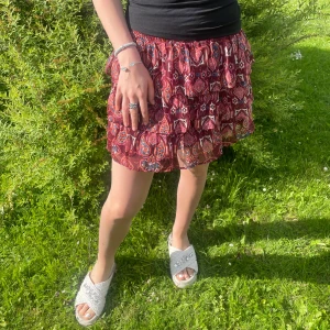 Röd volangkjol med paisleymönster - Supersöt kort kjol i rött med paisleyinspirerat mönster och flera volanger. Kjolen har resår i midjan och är luftig, perfekt för varma dagar. Färgerna går i rött, blått och vitt. Passar dig som gillar boho-vibe och vill ha något bekvämt men ändå snyggt. Från lindex barn men passar xs/s