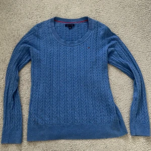 Blå kabelstickad tröja Tommy Hilfiger - Kabelstickad blå tröja från Tommy Hilfiger med rund halsringning och diskret logga på bröstet. Tröjan har långa ärmar och ribbade muddar. Perfekt för dig som gillar klassisk och stilren look.