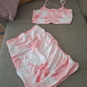 Vit och rosa tie-dye kjol & crop top - Säljer en kort kjol & croptop i vit och rosa tie-dye med rynkade detaljer på ena sidan. De har en mjuk och stretchig känsla, perfekt för varma dagar. Passformen är normal och tyget är tunt och följsamt.