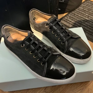 Lanvin - grå - Snygga gråa sneakers med ovandel i mocka och glansig, lackad tå. Skorna har svarta snören, guldfärgade öljetter och vit sula. Perfekta för dig som vill ha en stilren men ändå unik look.                                                 Allt og ingår!                                                  Priset kan möjligen sänkas vid en snabb affär! 💸
