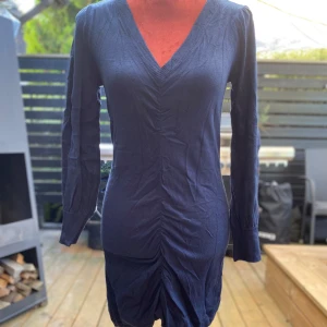 Mörkblå stickad klänning från b.young S - Mörkblå klänning med långa ärmar och V-ringning. Klänningen har en figurnära passform med rynkdetaljer framtill. Längd: 85 cm ﻿Bystvidd: 45 cm ﻿80% viskos ﻿20% polyamid  Inga bilder när den sitter på mig! Katter finns i hemmet!