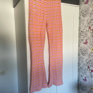 Stickat retrosett från new yorker - Säljer ett par stickade byxor och en topp från FB Sister i storlek L. Settet har ett färgglatt vågmönster i rosa, orange och vitt, med en mjuk och luftig stickad känsla. Byxorna är uppsydda lite lätt.
