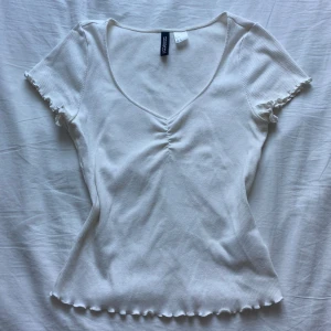 Söt ribbad topp - Supersöt vit ribbad topp från H&M Divided med v-ringning och rynkdetalj. Sitter figurnära och är petfekt till allt!