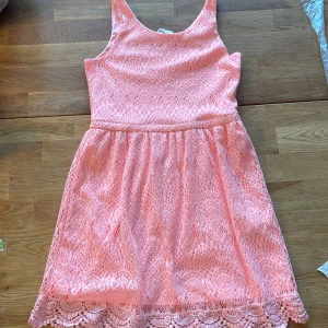 Rosa spetsklänning med volangkant - Superfin rosa kortklänning med spets och volangdetalj längst ner. Ärmlös modell med rund halsringning och markerad midja. Perfekt för sommarens alla tillfällen och ger en söt och fräsch look.