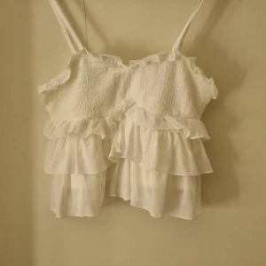 Vit volangtopp - Söt vit topp med smala axelband och volanger. Den är perfekt för sommaren, säljar för att jag aldrig använt den och känner att den kan komma till bättre användning hos någon annan