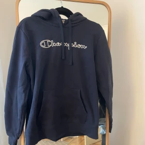 Mörkblå hoodie från Champion - Säljer en snygg mörkblå hoodie från Champion med deras ikoniska logga på bröstet. Tröjan har en klassisk känguruficka och justerbar huva med dragsko. Perfekt för en avslappnad stil. 🧢