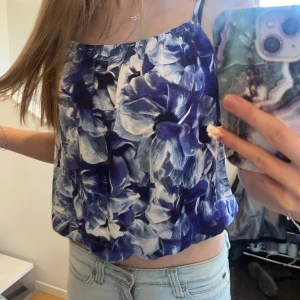 Blå blommig linnetopp - Snygg blå och vit blommig linnetopp med smala axelband. Perfekt för sommardagar och ger en fräsch look. Toppen har en luftig passform och är lätt att matcha med jeans eller shorts.
