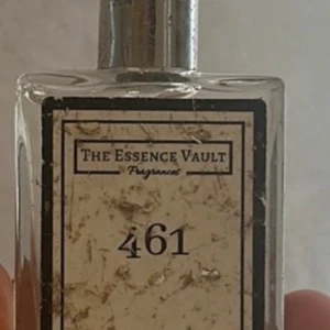 Parfym 461 från The Essence Vault - Säljer en elegant parfymflaska från The Essence Vault med nummer 461. Flaskan är rektangulär och genomskinlig med en silverfärgad spraypump. Etiketten har en stilren design med svart text på vit bakgrund. Perfekt för den som söker en unik doftupplevelse. Full flaska