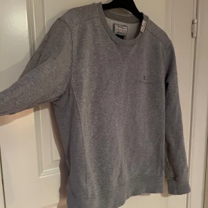 Grå sweatshirt från Champion - Säljer en klassisk grå sweatshirt från Champion Heritage. Tröjan har rund hals och långa ärmar med ribbade muddar. För liten för mig. 